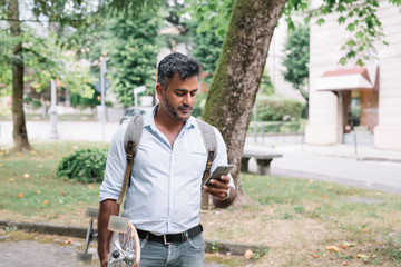 Casual businessman with skateboard using smartphone in the city