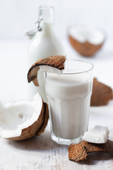 Fat free lactose free vegan drink: fresh coconut milk. Glass and bottle filled with healthy and sweet beverage, fresh coconut as decor to illustrate ingredients. Natural source of vitamins