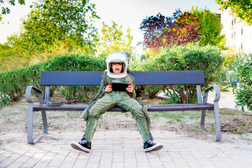 Boy wearing a space suit and sitting on a bench, using tablet