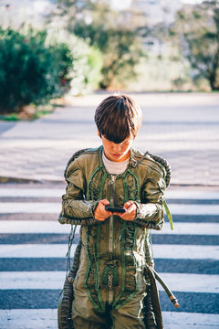 Boy wearing a space suit, crossing road and using smartphone