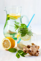 Healthy and tasty drink: homemade lemonade with lemon, mint, ginger in transparent glass mug with blue straw. Healthcare, concious lifestyle, detox. White background, copy space for text