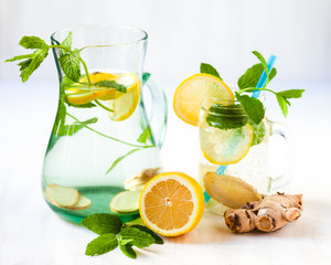 Healthy and tasty drink: homemade lemonade with lemon, mint, ginger in transparent glass mug with blue straw. Healthcare, concious lifestyle, detox. White background, copy space for text