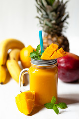 Refreshing summer cold mango ananas banana smoothie with fresh mint: low calories drink. Sweet fruity dessert for summer beach party.  In glass jar with blue straw. Slices of mango as decor