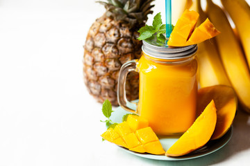 Refreshing summer cold mango ananas banana smoothie with fresh mint: low calories drink. Sweet fruity dessert for summer beach party.  In glass jar with blue straw. Slices of mango as decor