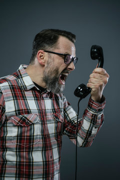 Man screaming into retro telephone in front of grey background