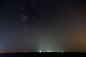Stars of the milky way galaxy in the night sky. The horizon is illuminated by the light of the city.