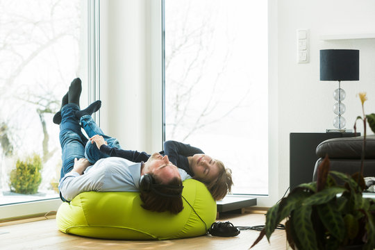 Father and son lying on bean bag in living room listening music