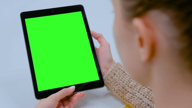 Woman looking at black digital tablet computer device with empty green screen on table at home, cafe or office. Technology, chroma key, template, mock up and entertainment concept