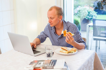 Man at home using his laptop while eating a snack