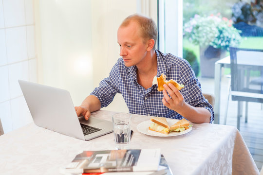 Man At Home Using His Laptop While Eating A Snack