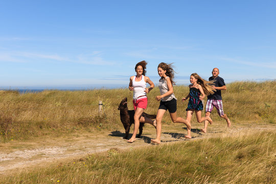 France, Bretagne, Ste Marguerite, Landeda, Finistre, parents and two daughters running with her dog on a dune at Atlantic