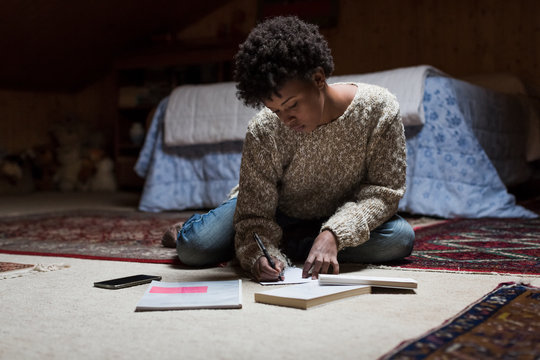Young woman at home sitting on floor writing