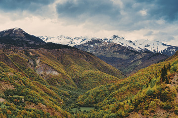 Beautiful mountain landscape, high snowy peaks, cloudy sky, forest.