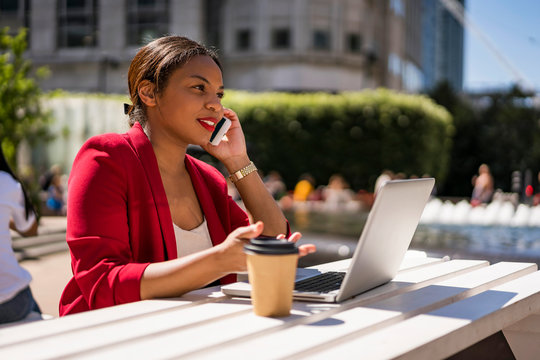 Businesswoman on the phone with laptop and coffee to go outdoors, London, UK