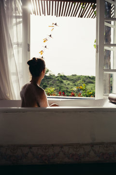 Woman relaxing in bathtub looking out of open window