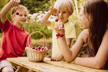 Three children holding up cherries in garden