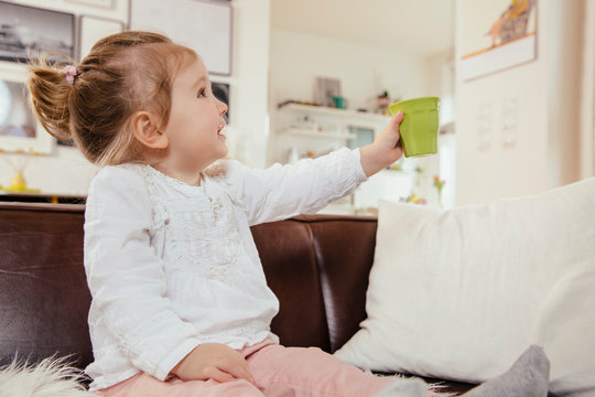 Little girl holding up a plastic cup while sitting on couch