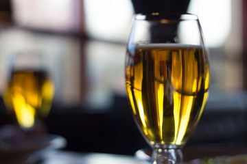 two graceful glasses of golden beer stand on a table against the background of a window in a cozy bar.