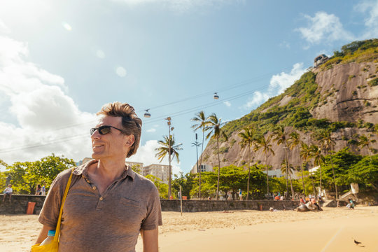 Brazil, Morro da Urca behind a male tourist on Praia Vermelha in Rio de Janeiro