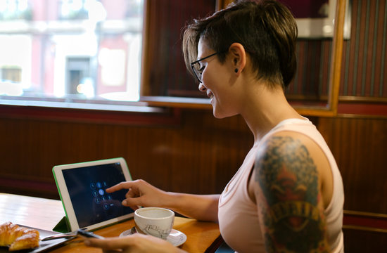 Tattooed young woman sitting in a coffee shop using digital tablet