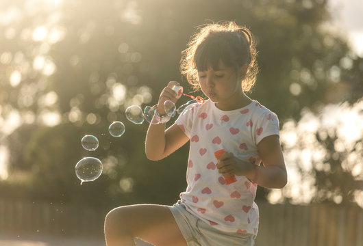Little girl making soap bubbles in the park at twilight