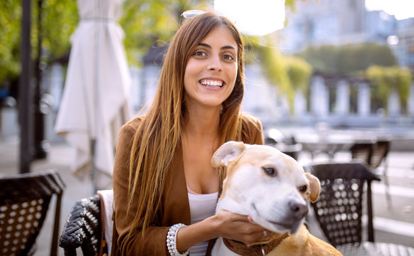 Spain, Gijon, Young woman sitting in pavement cafe, tickling her dog