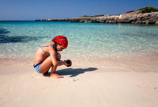 Spain, Balearic Islands, Menorca, little girl playing on the beach with a coconut husk