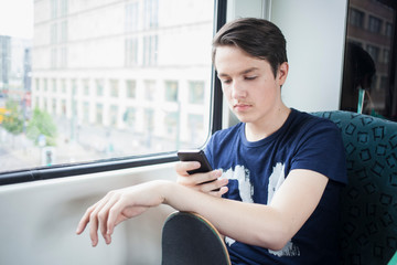 Teenage boy with skateboard sitting in commuter line using smartphone