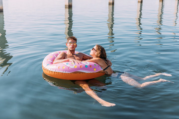 Young couple bathing in the sea on inflatable float in donut shape