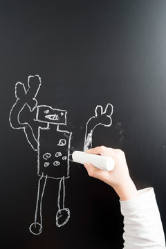 Little boy's hand drawing robot on a blackboard