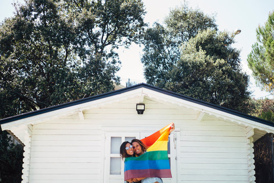 Two smiling woman holding up a rainbow flag