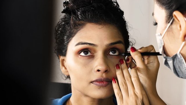 Beautiful young woman applying eyeshadow with a makeup artist in makeup room. Shot in 4k resolution