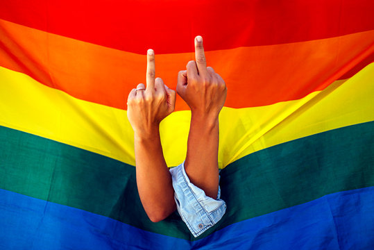Two women giving the finger in front of a rainbow flag