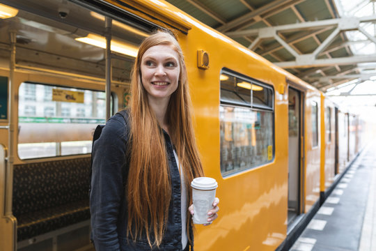 Portrait of redheaded young woman with coffee to go getting out of train, Berlin, Germany
