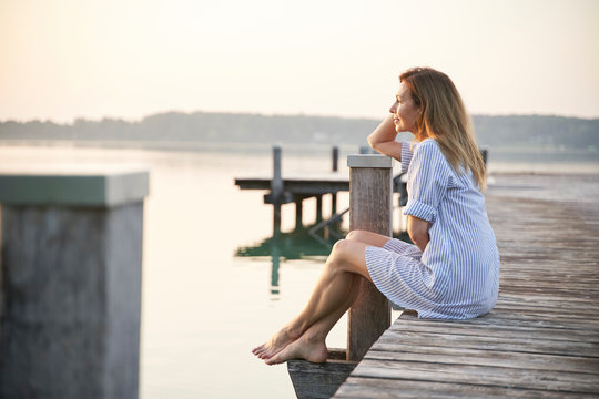 mature, woman sitting on jetty at a lake at sunrise