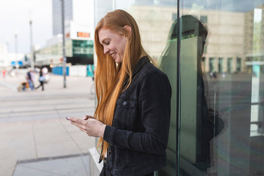 Redheaded young woman text messaging, Berlin, Germany