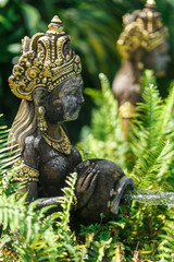 Fototapeta na wymiar Balinese statuette of a girl with a pot from which water flows. Pool decoration