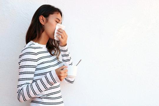 Young woman blowing nose into tissue