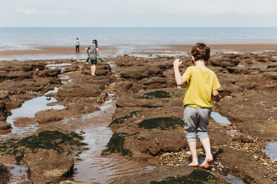 Boy walking over rocky seashore towards sea with family