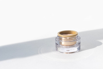 Glass shiny beauty jar with face cream with strong shadows on white background. Organic natural product for face care. Magazines, social media. Cosmetics, skin care, beauty concept. Copy Space