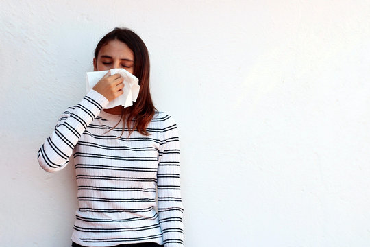 Young woman blowing nose into tissue