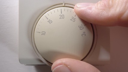 Close POV shot of a man’s fingers turning up the room thermostat for a domestic heating system to precisely 20 degrees celsius / centigrade.