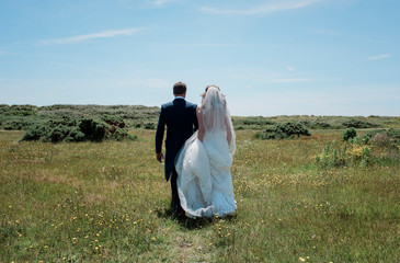 Bride and groom walking through a field of green on their wedding day