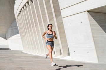 Full body of female athlete in sportswear running on concrete