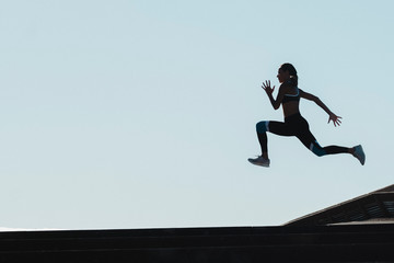 Silhouette of female athlete jumping against blue sky
