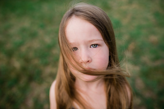 Close up of serious girl in grass looking at camera wind blown hair