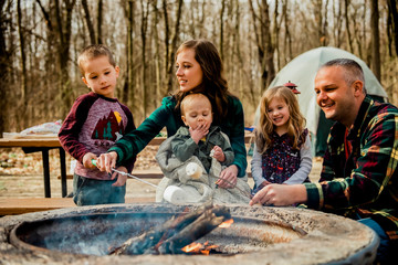 Smiling family roasting marshmallows over campfire in woods during autumn