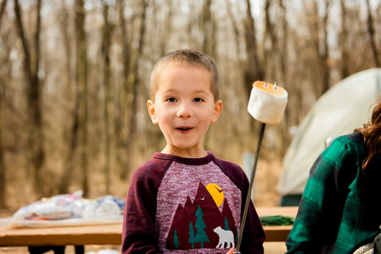 Excited boy holds up cooked marshmallow on stick at campsite in Fall