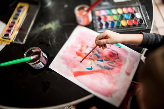 young child's hand painting with a brush surrounded by art supplies