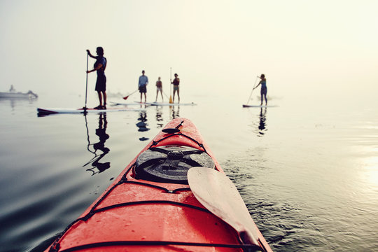 A group of standup paddle boarders and kayakers on a foggy morning